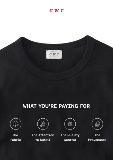 Close-up of a black crewneck t-shirt with a white printed graphic reading 'WHAT YOU'RE PAYING FOR' above four circular icons and text describing fabric, attention to detail, quality control, and provenance. A small CWT label is visible inside the collar, and 'CWT' appears in red at the top of the image.