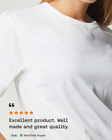 A close-up of a person wearing a plain white crew-neck T-shirt against a light neutral background, with a review overlay on the lower left praising the product.